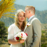 Wedding portrait of the bride and groom smiling at each other, dressed in wedding attire, with a natural outdoor background.